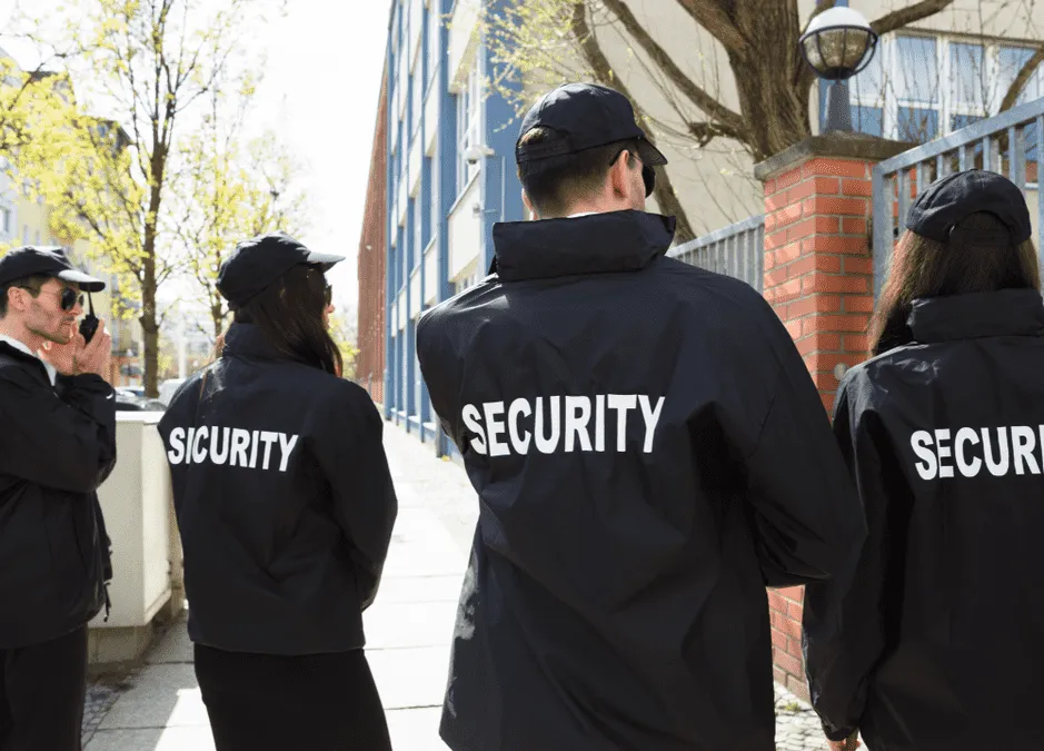 A group of security personnel in black jackets with "SECURITY" printed, standing together outdoors in a city setting.
