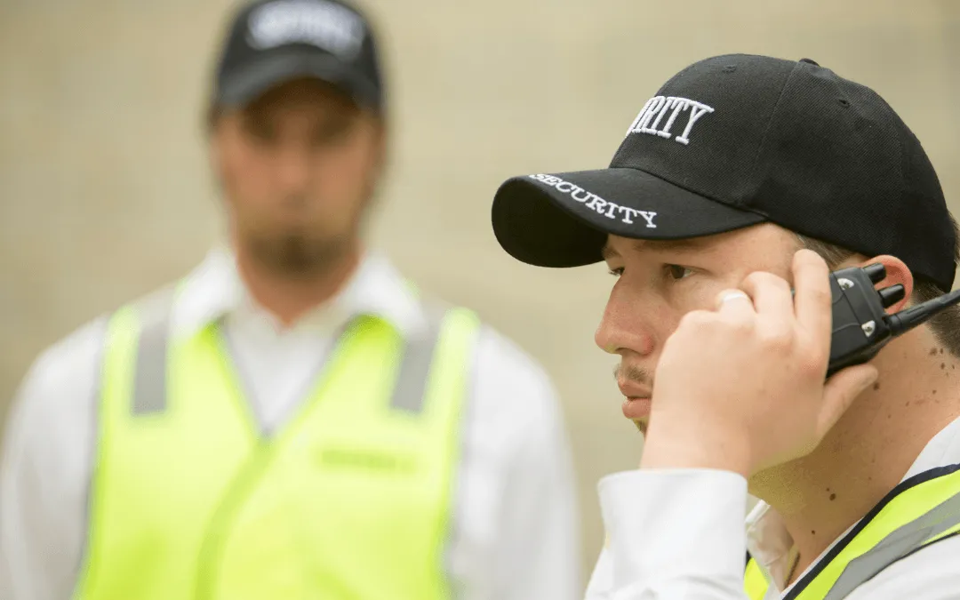 Two security personnel are present, one speaking into a radio and wearing a cap with "SECURITY" on it, while the other stands in the background, also in a security outfit.